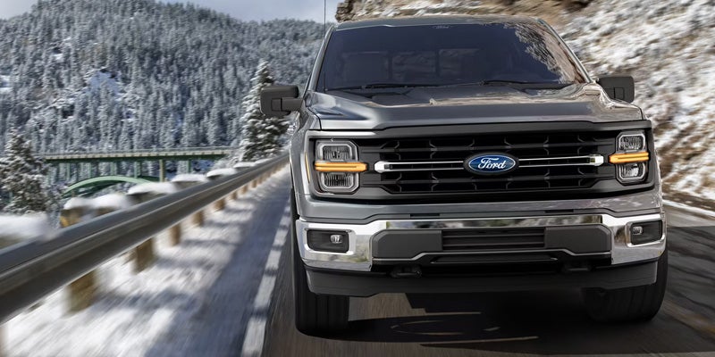 A Ford F-150 drives along a snowy mountain road, showcasing its rugged capability in winter conditions.