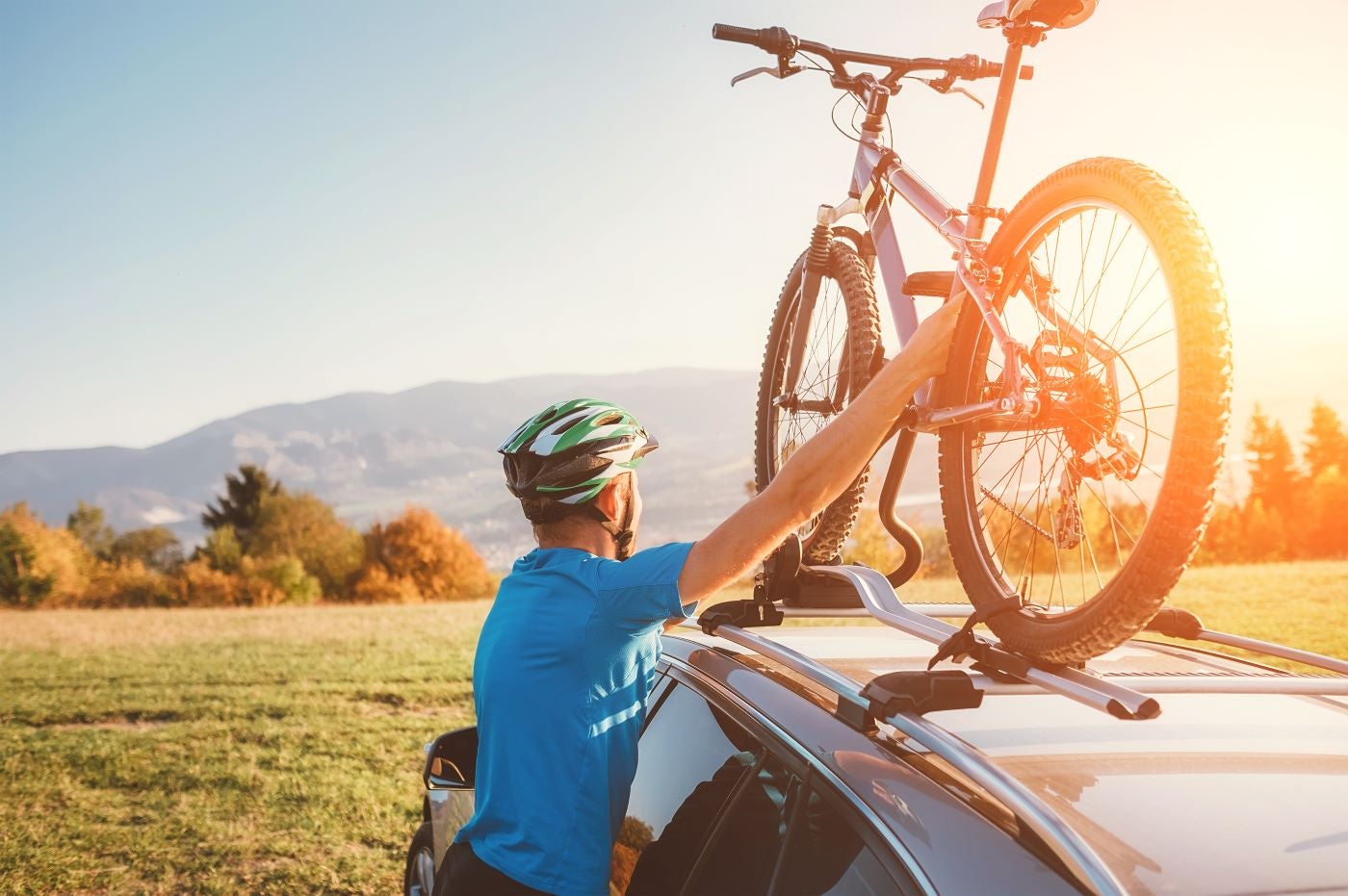 A man secures his bike on top of his car, preparing for a cycling trip.